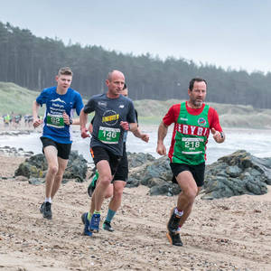 Three runners race on Llanddwyn beach in the Anglesey Trail Half Marathon